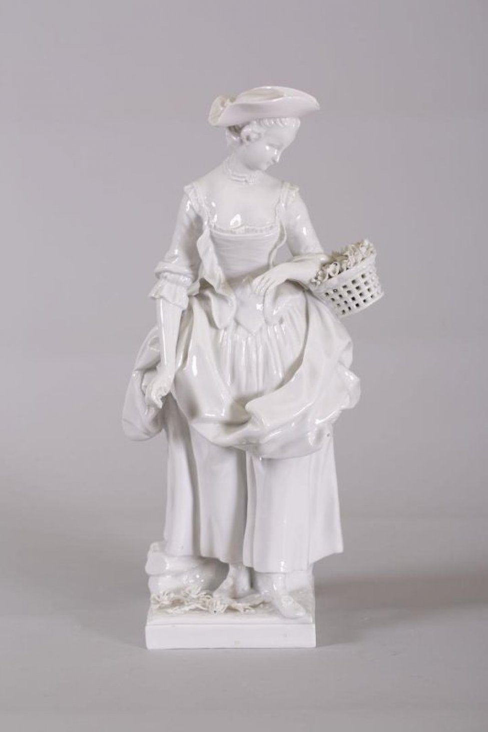 Изображена женщина в костюме 18 века, в треугольной шляпес поднятыми полями. На левой руке- корзинка с лепными  цветами, в опущенной вниз правой- цвеок. На постаменте- лепные цветы.