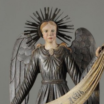 Ангел стоит в нижнем ряду слева в рост. Изображен с поднятой левой рукой и опущенной правой. Одежды: верхняя - позолочена, нижняя - посеребрена. Крылья опущенные, посеребренные.