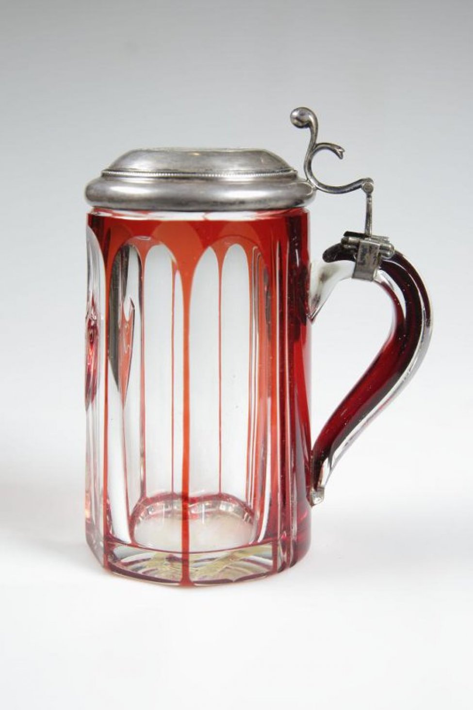 Кружка из двухслойного стекла (белое с красным), шестигранная, со щитком красного цвета. На стеклянной ручке укреплена серебряная крышка, в которую вмонтирован рубль 1724 г. с изображением Петра I.