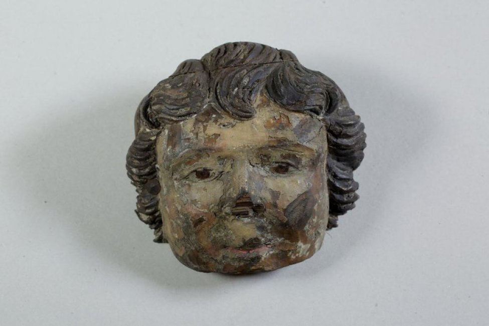 Детали на лице имеют невысокий рельеф. Верхняя часть головы выполнена в куске дерева, плохо прикрепленном к остальной скульптурной массе.