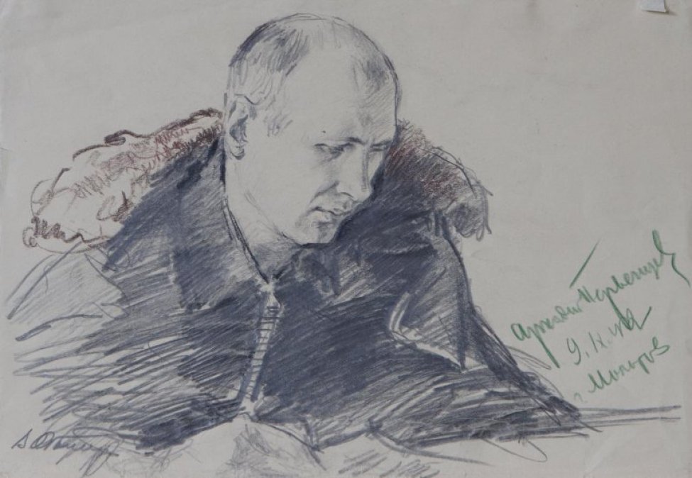 Погрудное изображение молодого мужчины сидящего за столом с бумагой в руках; на плечи накинуто пальто.