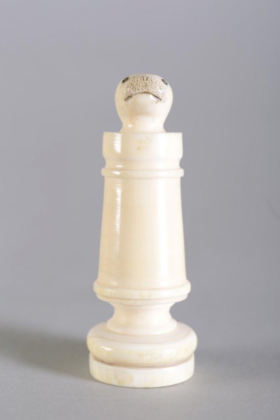 Шахматная фигура белого цвета в виде цилиндрической профилированной балясины, вверху заканчивается головой нерпы. На голове неглубокой резьбой (процарапыванием) с черной тонировкой обозначены  маленькие круглые глаза, линия рта и точки на морде. Вся фигура выполнена из одного куска бивня.