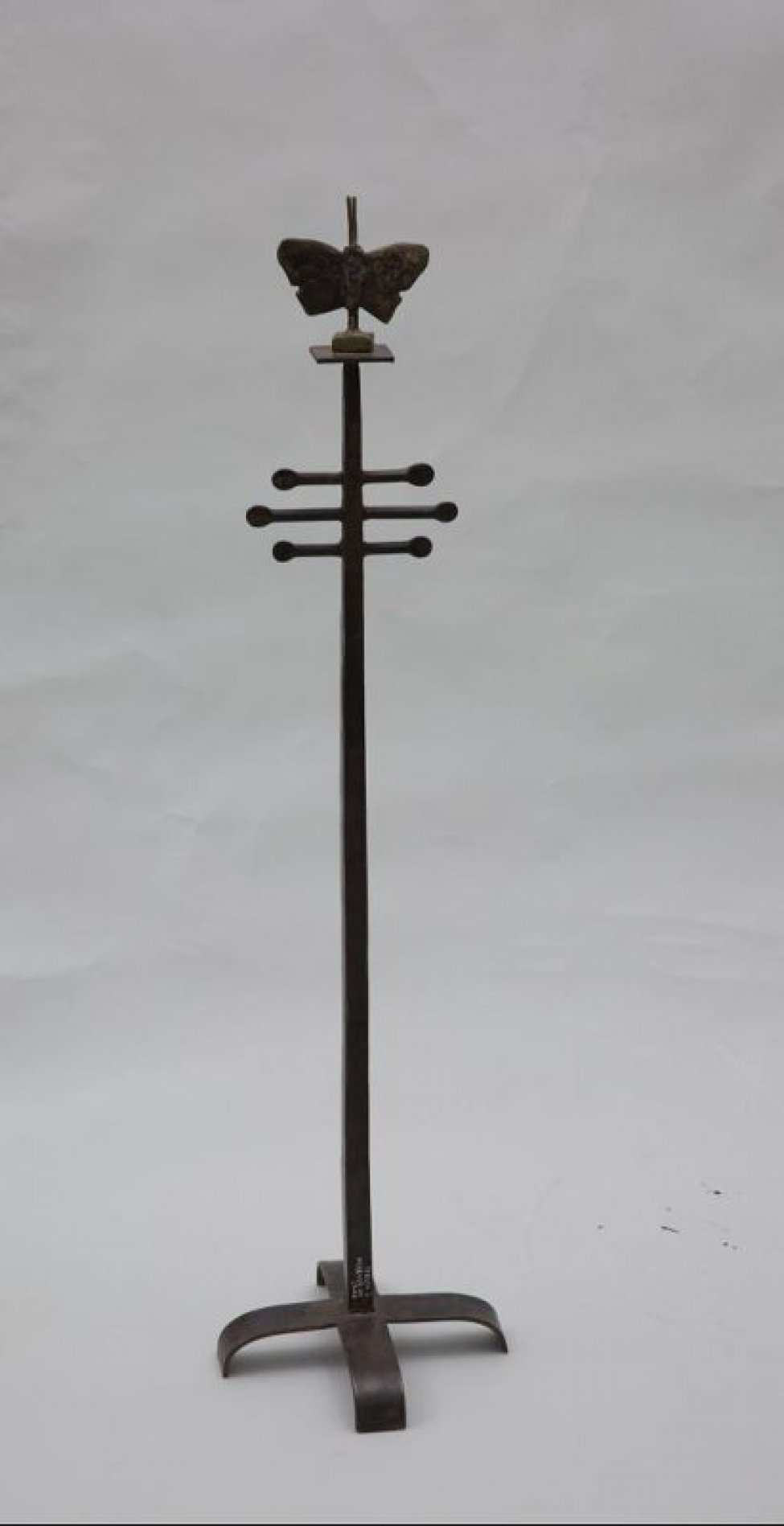 На крестообразном основании на вертикальном стержне с подставкой изображена бабочка со смещением наискось с длинными усиками.