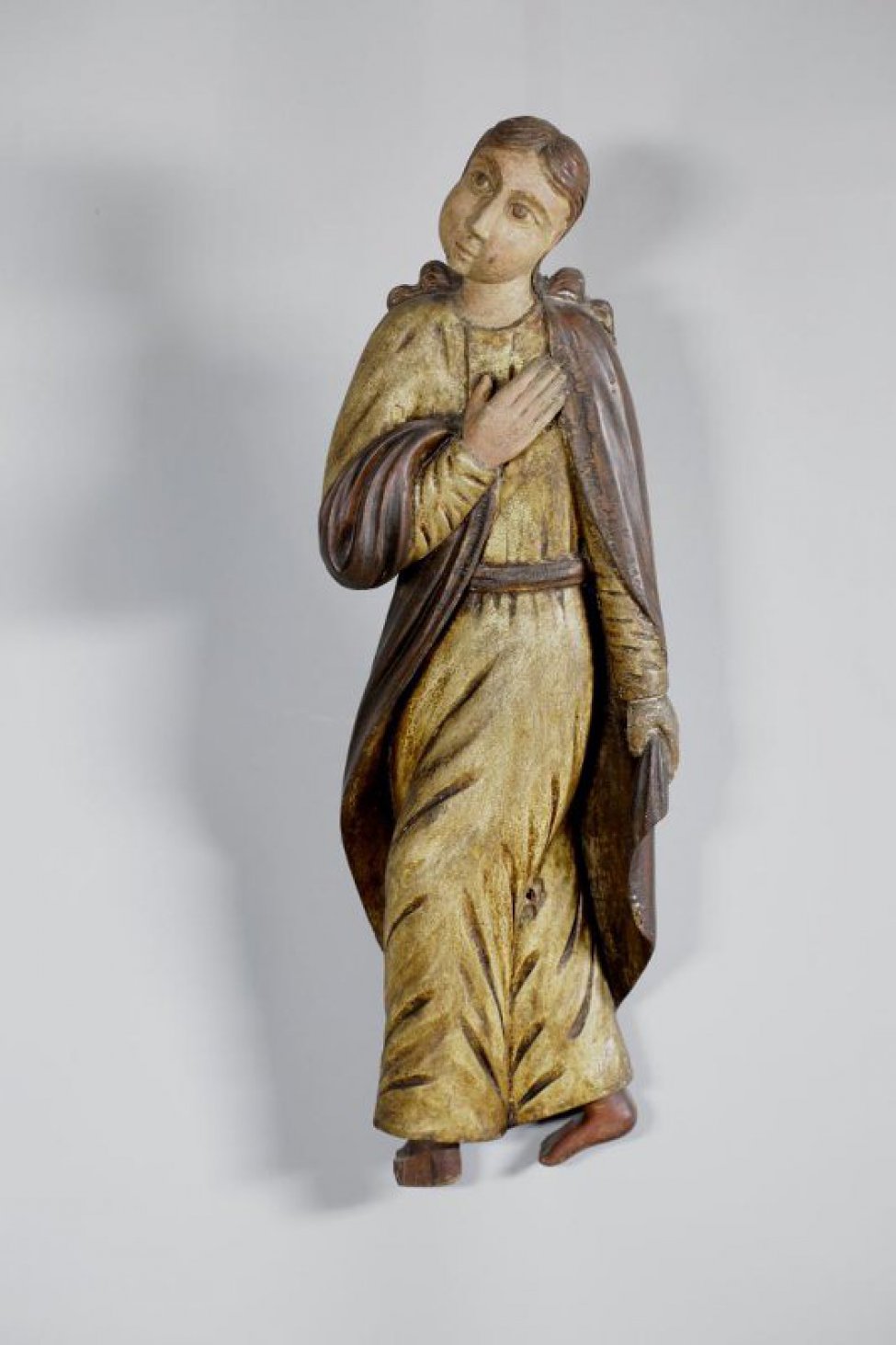 Иоанн Богослов изображен во фронтальном положении корпуса, ноги вырезаны идущими вправо, к кресту. Правая рука лежит на груди, левая опущена. Позолоченный хитон покрыт посеребренным гиматием.