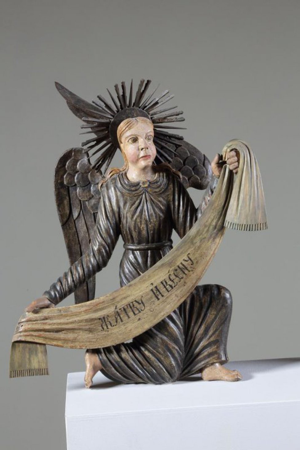Ангел коленопреклоненный, стоит в нижнем ряду справа. Изображен с поднятой левой рукой и опущенной правой. Одежда посеребрена. Крылья опущенные, посеребренные.