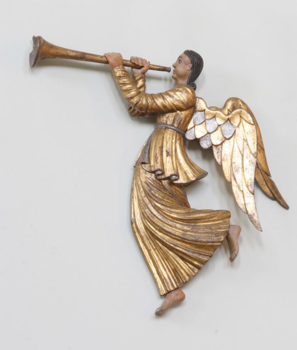Летящий ангел с трубой в руках. Скульптура изображает ангела в левый профиль и по композиции имеет обратный перевод с ДС-224, с которой аналогична и по характеру выполнения. Фигура изогнута движением вперед (вправо) так, что ноги откинуты назад (влево), особенно левая нога. Руки вытянуты вперед и подняты на уровне плеч. На позолоченных одеждах частые мелкие складки, развевающиеся назад. Верхняя одежда с поясом оканчивается у бедер, нижняя - у ступней ног. Отдельно вырезанные позолоченные крылья опущены. Ступни ног и руки от локтей вырезаны в присоединенных к основной скульптурной массе отдельных кусках дерева.