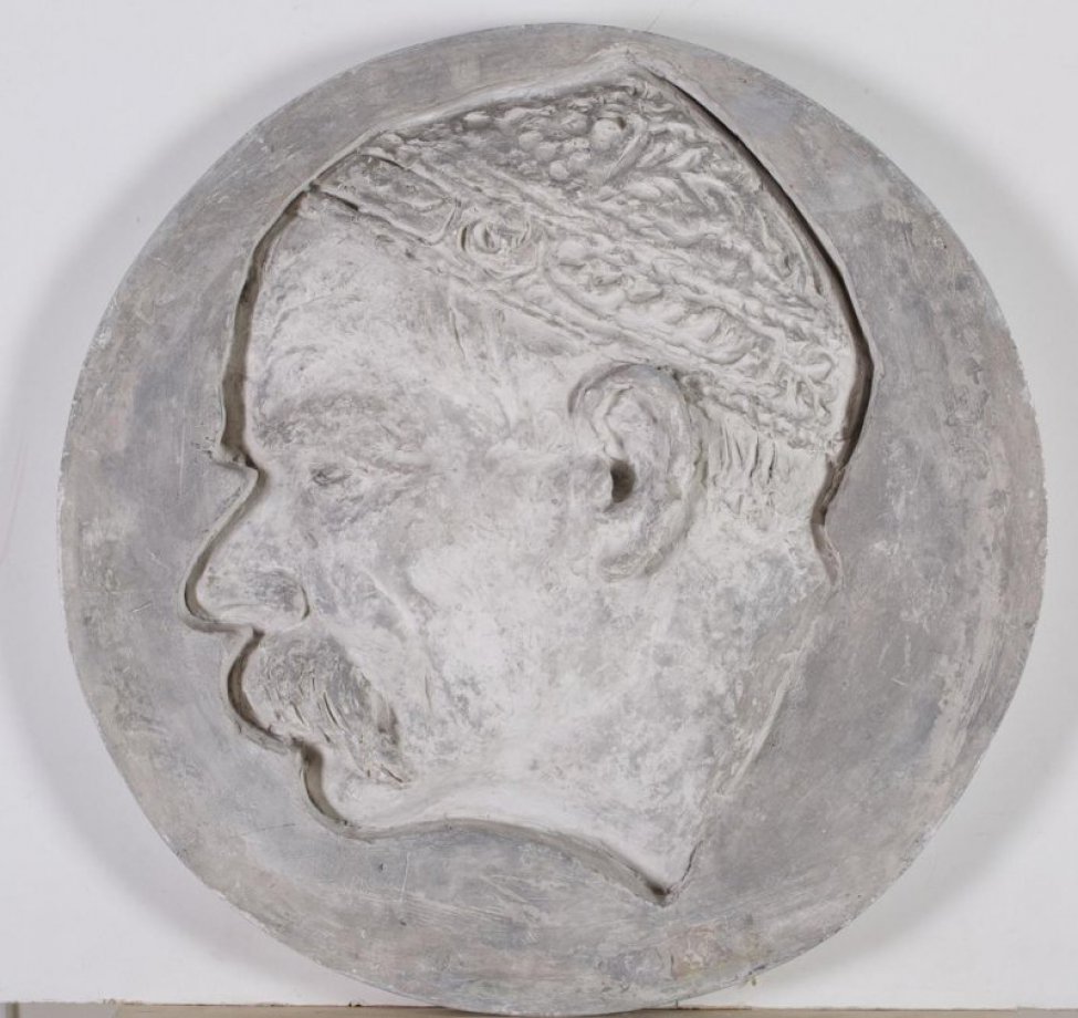 Изображена голова мужчины  в левый профиль. У мужчины глубоко посаженные глаза, длинные усы,  на голове  тюбетейка. Рельеф врезан в фон, оставляя у контура форм толщину слоя гипса.