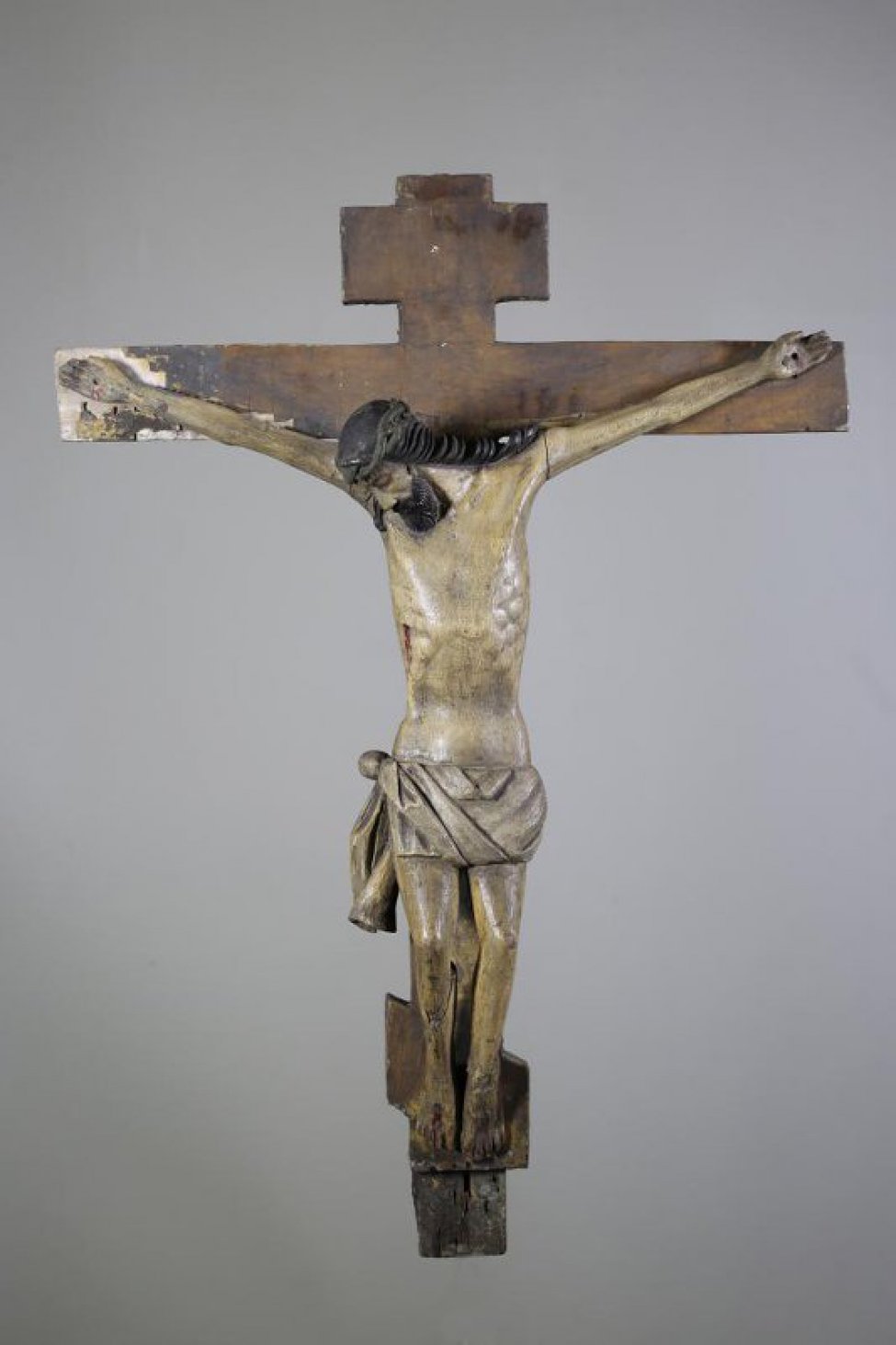 Фигура Распятого Христа вырезана в малоокруглых почти не детализированных поверхностях. Чресленник лежит изогнутыми плоскими складками, конец его свешивается завиваясь. Крест - коричневый, восьмиконечный.