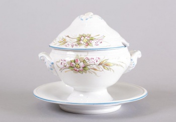 Соусница белого цвета в виде вазона на ножке с высокой крышкой, рельефными ручками, стоит на тарелке-поддоне; роспись цветочная.