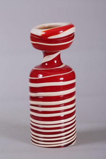 Подсвечник красного цвета с многочисленными горизонтальными белыми разводами;основание круглое, корпус цилиндрический, переходящий в узкое горлышко с широким полым навершием