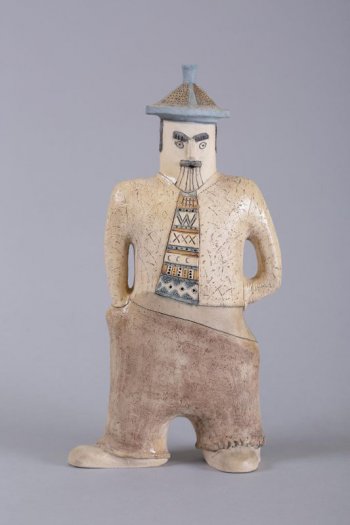 Стилизованная фигура мужчины с широко расставлеными ногами, в бежевых брюках и цветном галстуке; на голове круглая с четырехгранником и острым завершением шляпа.

