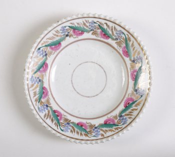 Тарелка мелкая, с рельефным горошчатым краем, белая. Борт расписан цветочным орнаментом из красных и синих цветов, зеленых и золоченых листьев.