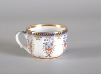 Чашка чайная, белая. Тулово расписано цветочным орнаментом  с золотыми с синим листьями. По краю тулова - орнаментальные золоченые каемки  на синем фоне. Внутри по краю золоченая каемка.