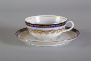 Чашка маленькая, белая. Тулово расписано золоченой орнаментальной каймой и синей каймой с золоченым растительным орнаментом.