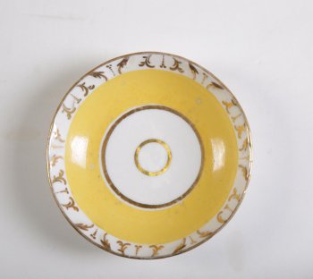 Блюдце чайное, желтое. По краю рельефная золоченая орнаментация лиственного характера.