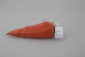 Обобщенное изображение моркови оранжевого цвета с темно-коричневыми точками, две стороны более плоские. Сверху короткая зеленая веточка, на которой треугольное крепление.