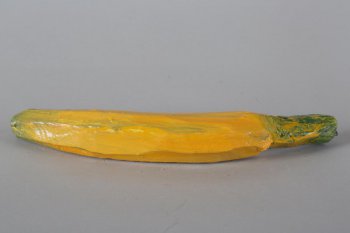Обобщенное изображение банана желтого цвета с зелеными разводами, с длинной желто-зеленой веткой, к которой прикреплена металлическая петелька.