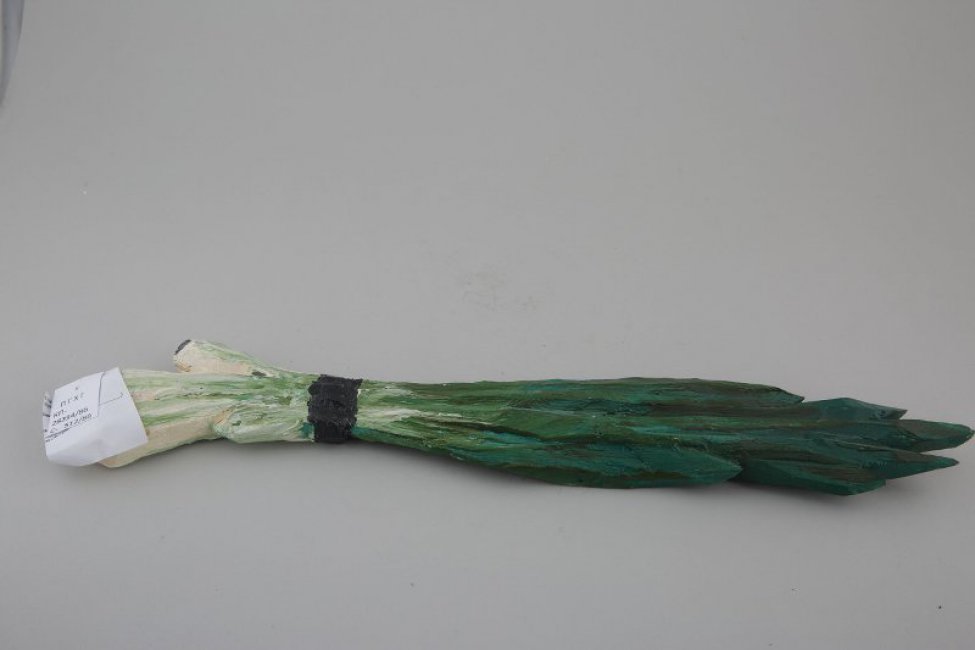 Обобщенное изображение перьев зеленого лука, стянутых черными нитями, с 4 бело-зелеными головками с черными концами и длинными темно-зелеными перьями. На одной из головок треугольное крепление.