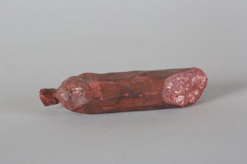 Обобщенное изображение части палки копченой колбасы в оболочке темно-коричневого цвета с темно-розовыми мазками. С одной стороны - 
