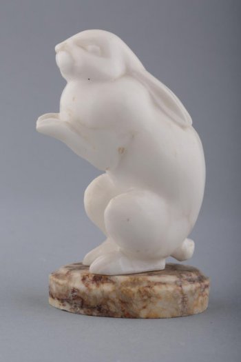 Кролик белый сидит на задних лапках, передние подняты вверх, голова втянута в плечи, уши прижаты к спине.