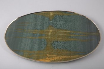 Овальной формы из серо-зеленого камня с коричнево-бежевыми полосами, в металлической оправе.