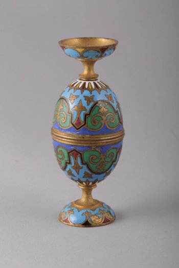 В форме яйца (состоит из 4-х частей: двух полусфер, двух ножек); украшена стилизованным растительным орнаментом восточного характера. Эмаль зеленого, синего, голубого, красного и белого цветов.