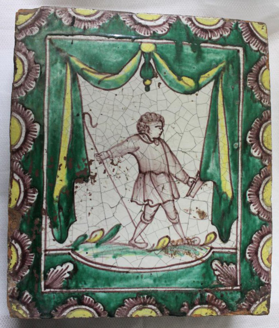Изразец с изображеним мужчины, в откинутой назад правой руке которого тонкая трость, в левой - прямоугольный предмет.