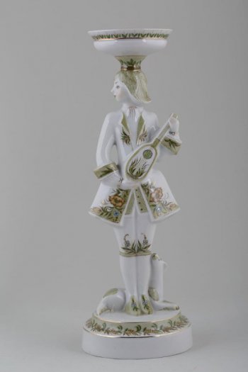 Скульптурное изображение юноши на круглом постаменте, с вазоном на голове, у ног - лежащая собака, в руках музыкальный инструмент. Камзол, вазон и постамент расписаны цветочным орнаментом.