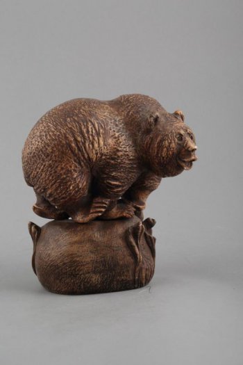 Фигура медведя на округлой, стилизованной под кочку с листьями, подставке. Медведь  изображен в левом повороте, с открытой пастью.