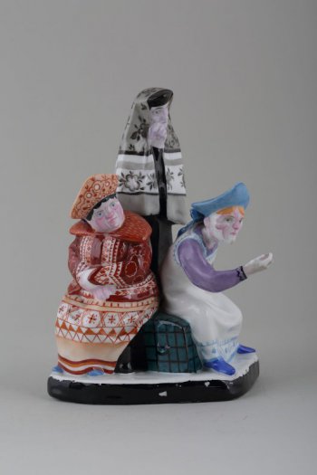 На постаменте изображены три женские фигуры в древнерусских костюмах с кокошниками на головах. Две женщины сидят на сундуке, одна стоит. Одежда расписана узорами, чёрной, голубой, сиреневой, красно-коричневой красками.