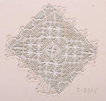 Ажурная квадратная салфеточка из белых нитей с зубчатыми краями. Ажурный фон заполнен звёздочками. В центре - рельефный крестик. Образец пришит к картонному листу.