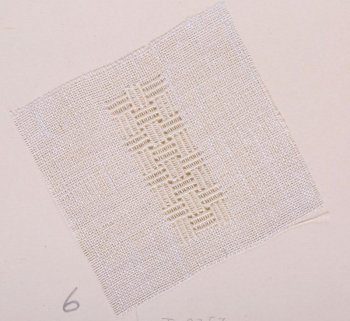 На образце квадратной формы из ткани редкого переплетения серого цвета в центре дана ажурная вышивка белым шёлком: группы по три рельефных столбика образуют шахматный узор. Образец приклеен на картонный лист.