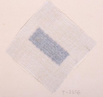 На образце квадратной формы из ткани редкого переплетения серого цвета в центре дан прямоугольный образец вышивки: серыми шёлковыми нитями в разных направлениях шиты квадратики, образующие шахматный узор. Образец приклеен на картонный лист.