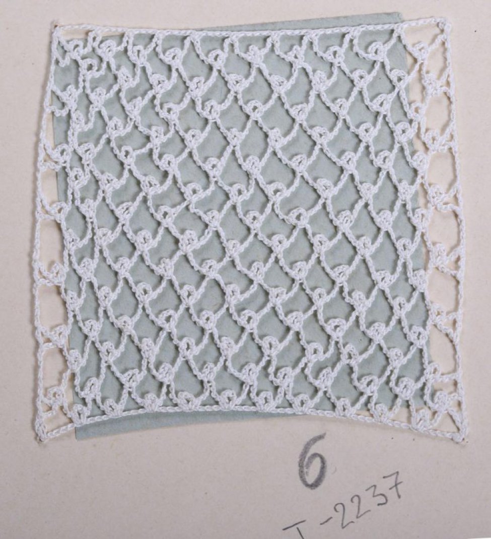 Образец прямоугольной формы, белого цвета, в виде сетки с петлей в нижнем углу. Образец пришит к картонному листу.