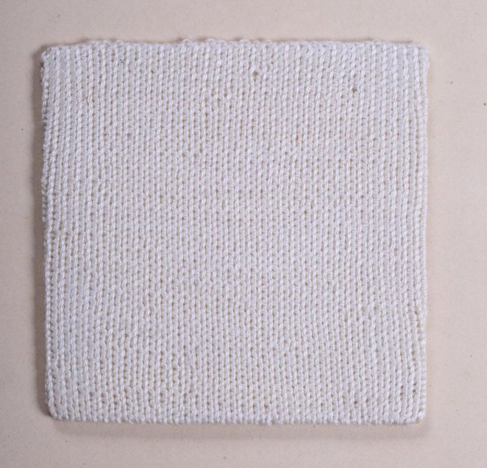 Образец квадратной формы из белых нитей выполнен в технике вязания лицевыми петлями. Образец натянут на картонку и пришит к картонному листу.