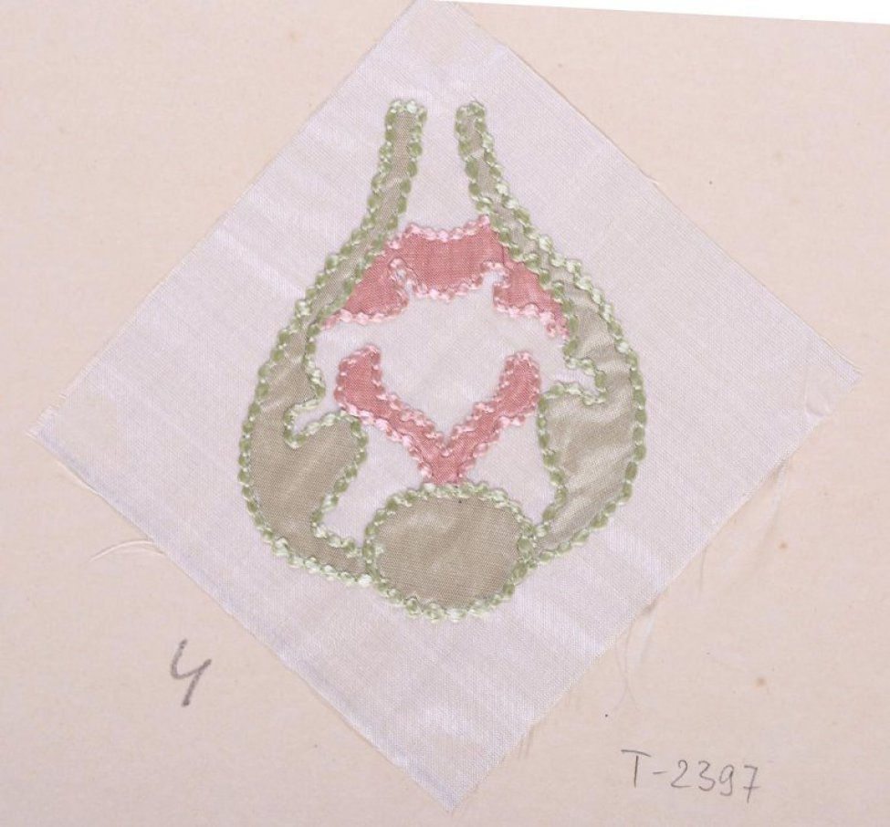 На белом шёлке квадратной формы в технике аппликации вышита светло-зелёная фигура в виде бутона. Внутри неё - аппликация из розового шёлка. Ткани аппликации обшиты зелёными и розовыми шёлковыми нитями. Образец приклеен к картонному листу.