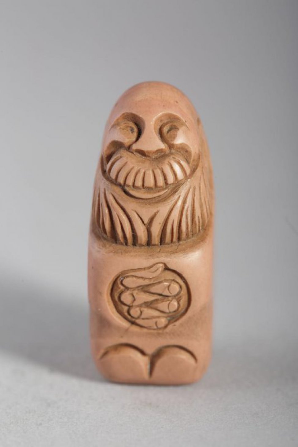 В форме прямоугольного блока, обработанного с одной стороны резьбой с изображением в рост бородатого, лысого, улыбающегося старца со сложенными на груди руками.