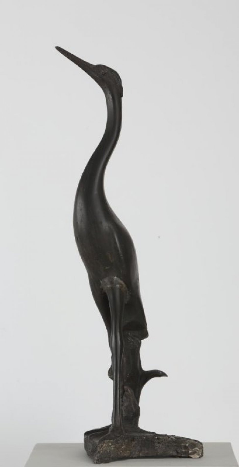 На плинте неправильной формы изображена стоящая черная цапля с длинной вытянутой шеей и поднятым вверх клювом.