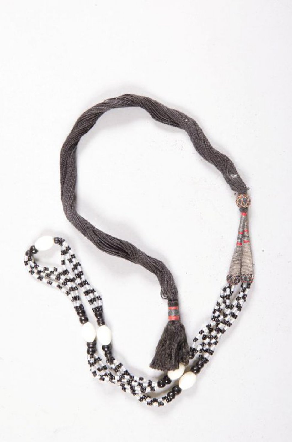 Четыре нитки белого и черного бисера с пятью большими белыми бусинками укреплены на черном шнурке с кисточкой.