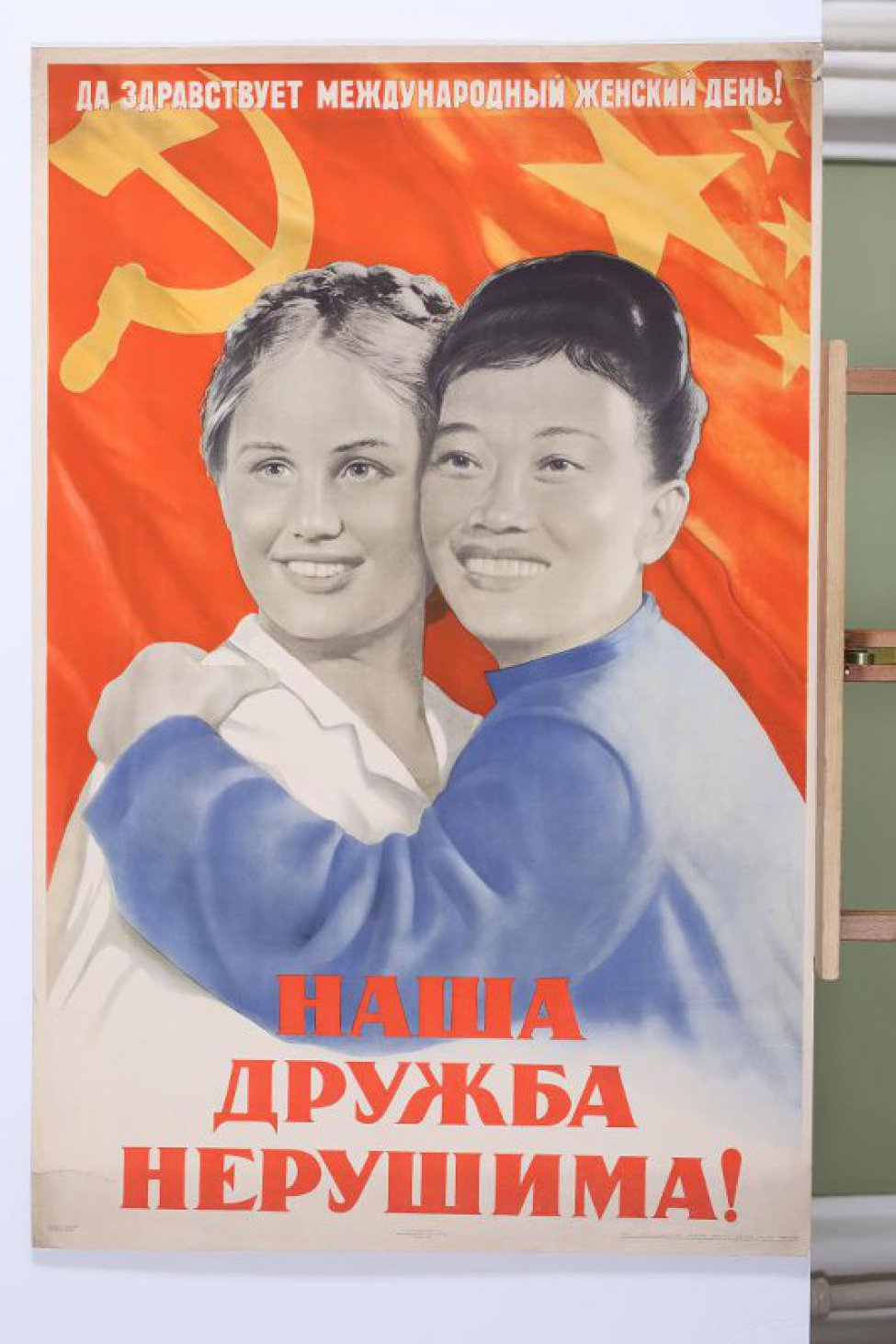 Изображена китайская женщина в синей одежде, обнимающая русскую женщину в белой кофте. Наверху текст: " Да здравствует международный женский день!"