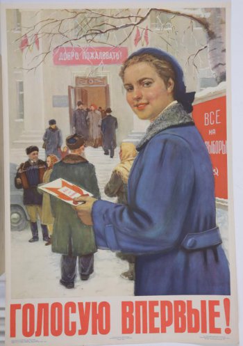 Изображена молодая девушка в синей шапочке и синем пальто. В левой руке она держит открытку- плакат 