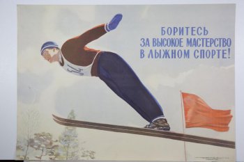 Изображён мужчина, делающий прыжок на лыжах. Он в синей шапке, синих рукавицах и синих брюках. На груди № 