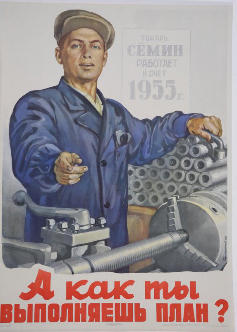 Изображен рабочий в синей спецовке, стоящий у станка. Правой рукой он показывает на надпись плаката, левой опирается на груду деталей, лежащих около него. Справа вверху надпись: " Токарь Семин работает в счет 1955 года".