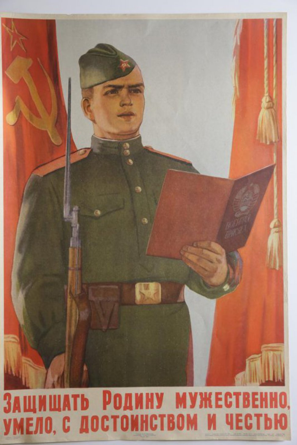 Изображен молодой солдат с винтовкой в правой руке; в левой руке он держит текст  воинской присяги. Под изображением надпись.