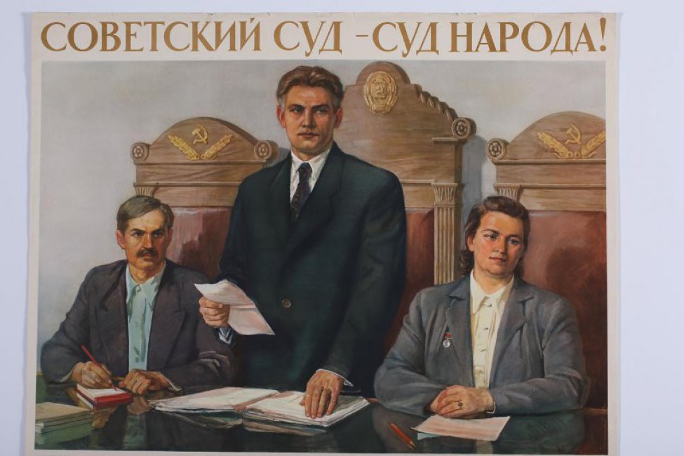 Изображены трое. В центре за столом мужчина с бумагами в правой руке, левая опирается на книгу. Справа от него - пожилой  мужчина ,слева молодая женщина. вверху над изображением: " Советский суд- суд народа!"