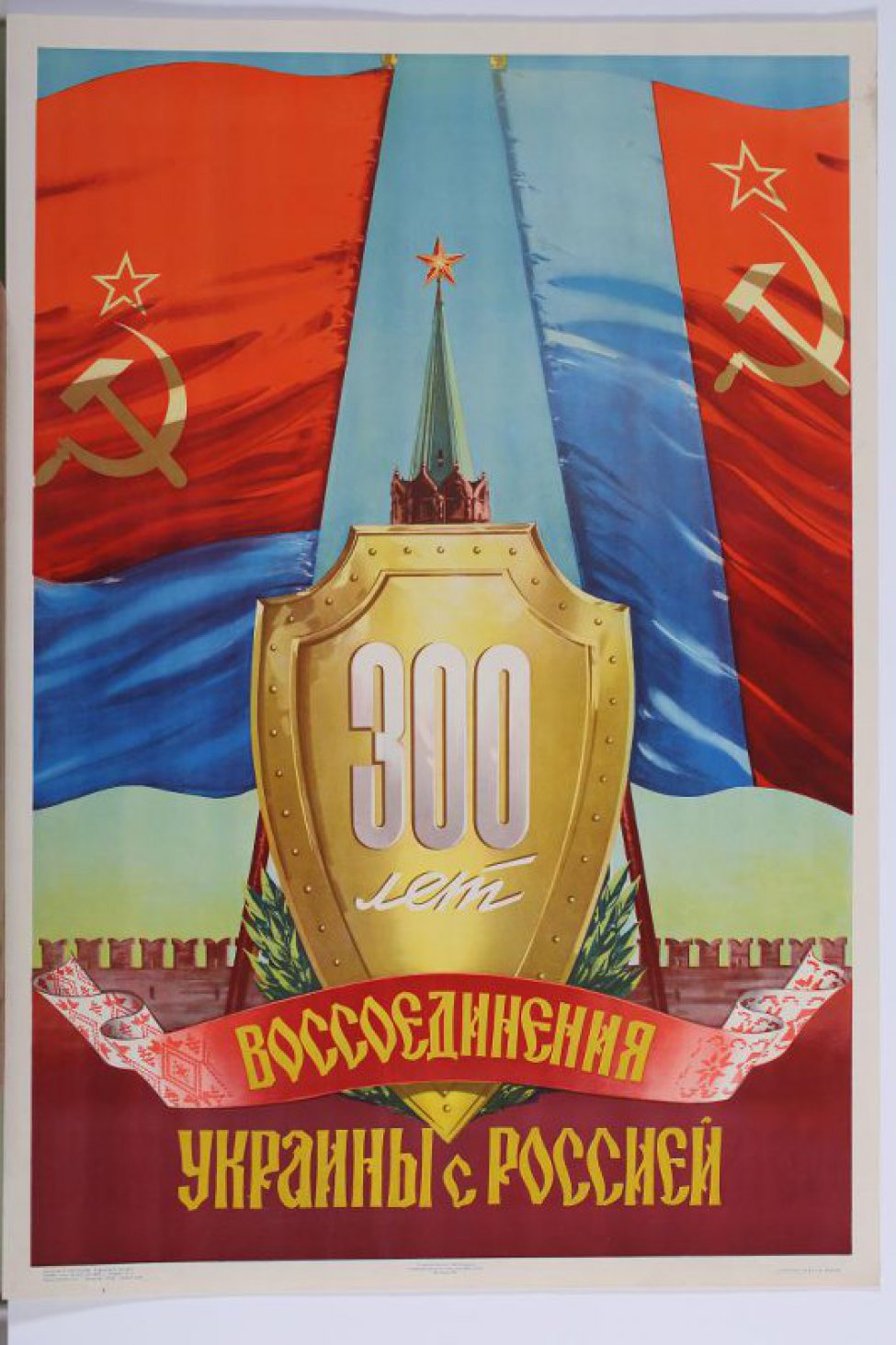 На щите, из под которого  видна верхняя часть Кремлевской башни написано " 300 лет", далее на ленте древне- русским шрифтом " воссоединение" и на фоне кремлевской стены             " Украины с Россией" . Вверху два красные, с синими полосами, знамени.