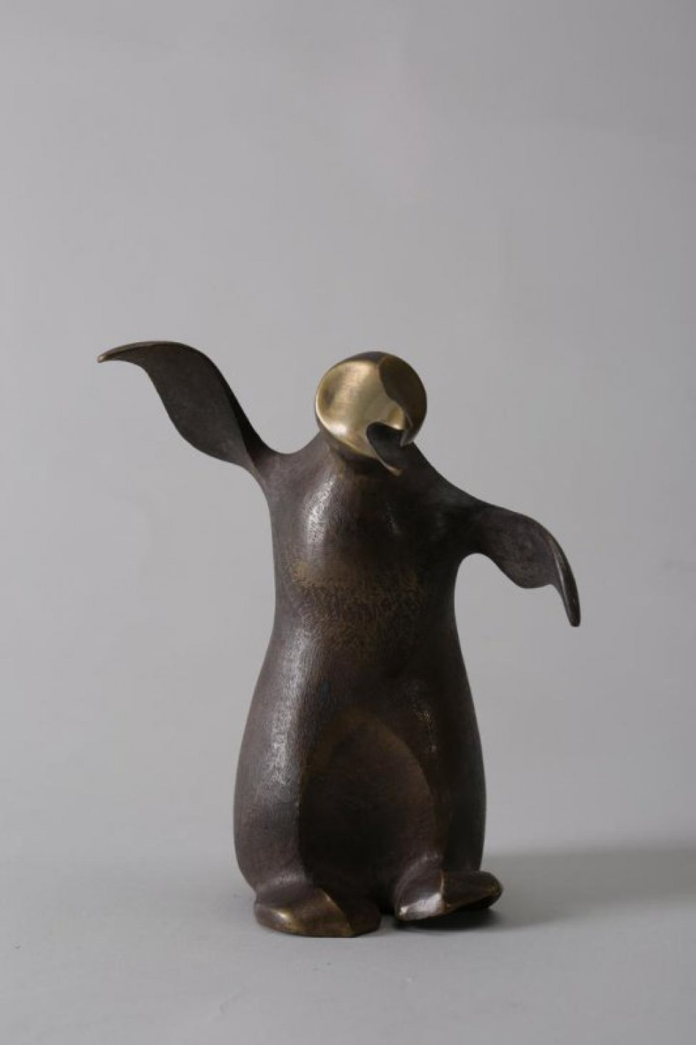Обобщенно трактованная фигура пингвина, вытянувшего голову с открытым клювом; крылья широко расставлены, правое поднято выше левого.