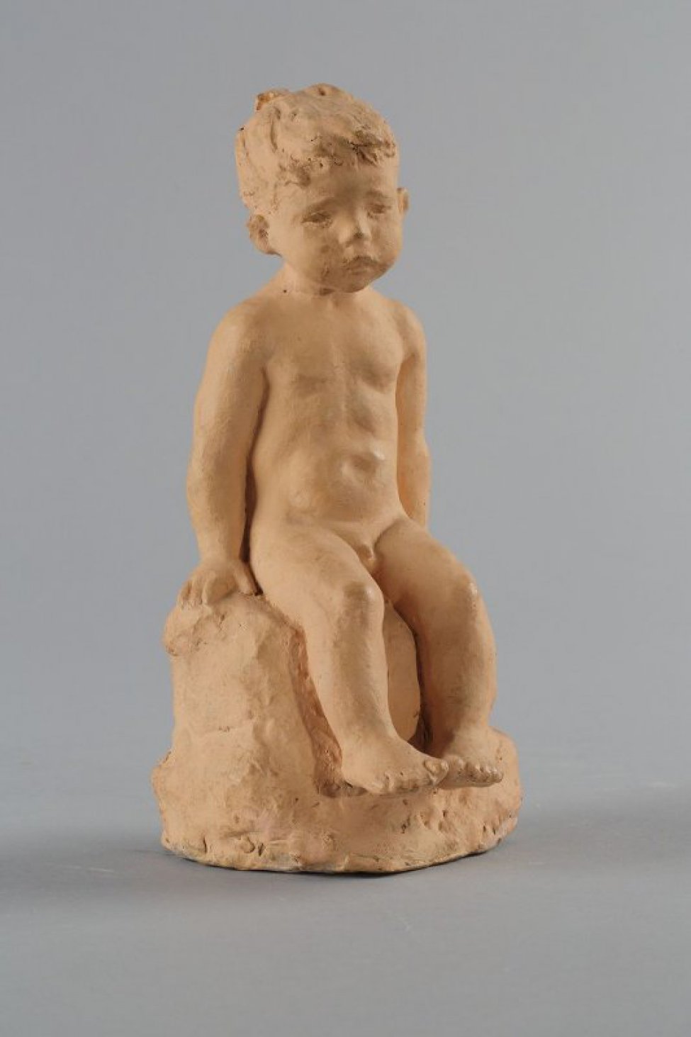 Изображен сидящий на камне обнаженный мальчик, руками опирается на камень, на котором сидит. Голова мальчика с короткой стрижкой наклонена вправо. Ступни ног соприкасаются большими пальцами.
