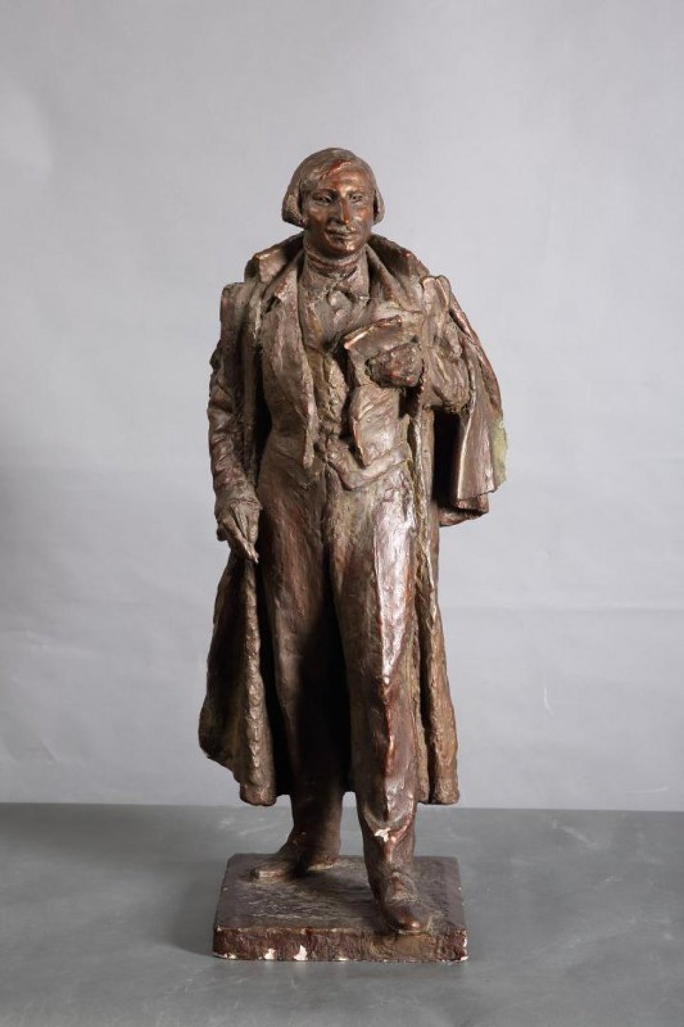 Гоголь изображен в рост, в накинутой на плечи верхней одежде, без головного убора. В левой руке у груди - раскрытая книга, в правой, опущенной вниз - карандаш. На постаменте.
Обрамление: Постамент квадратной формы.
