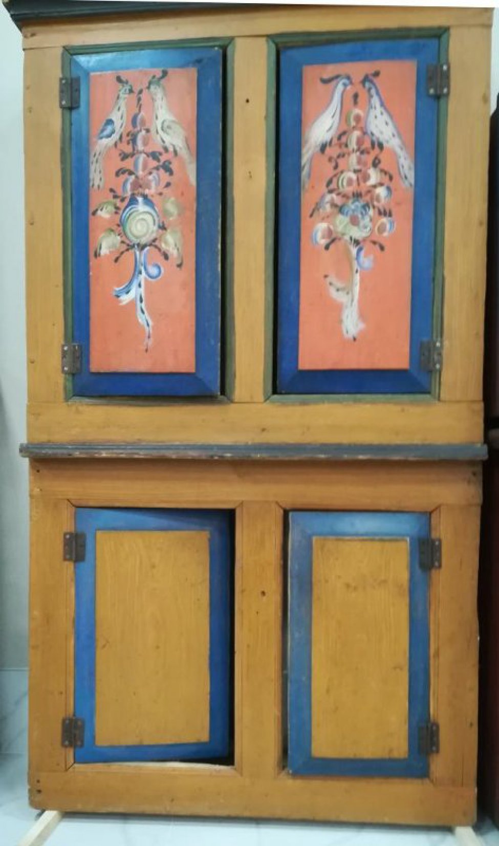 Двухсоставной, коричневый, вверху 2 дверцы расписные: на красном фоне на цветах 2 птицы, обведеные синей каймой. Внизу две дверцы без росписи с синей каймой.